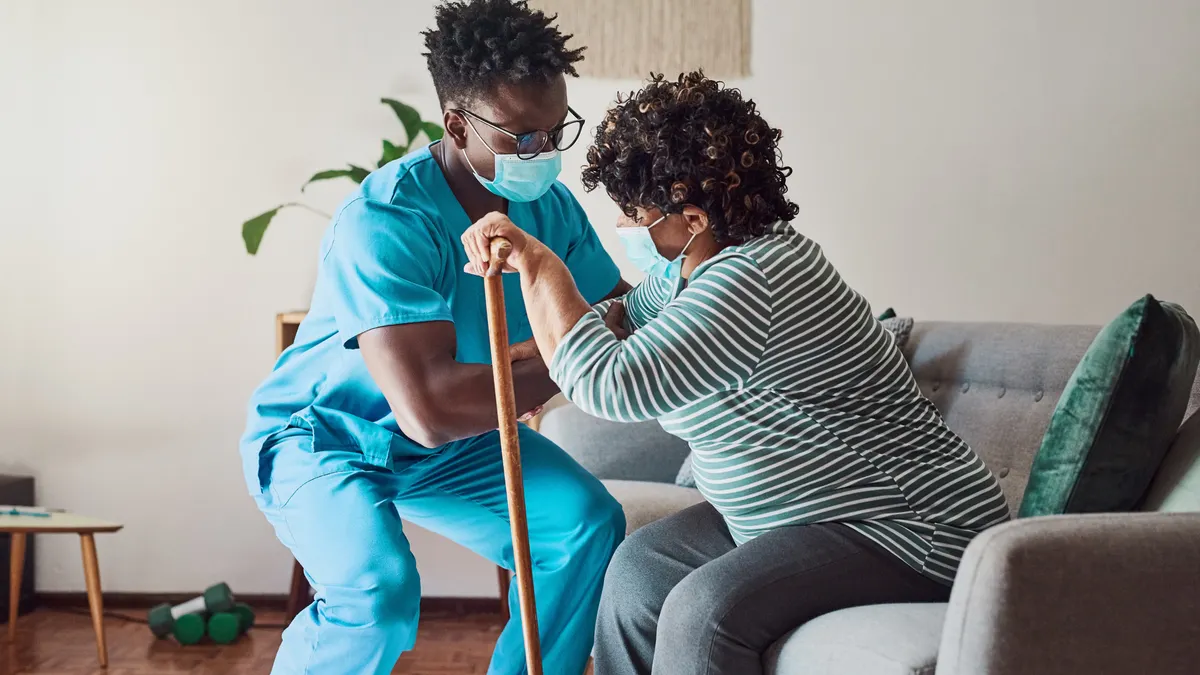 Clinician steadies an older adult while standing at home, checking for dizziness and safety.